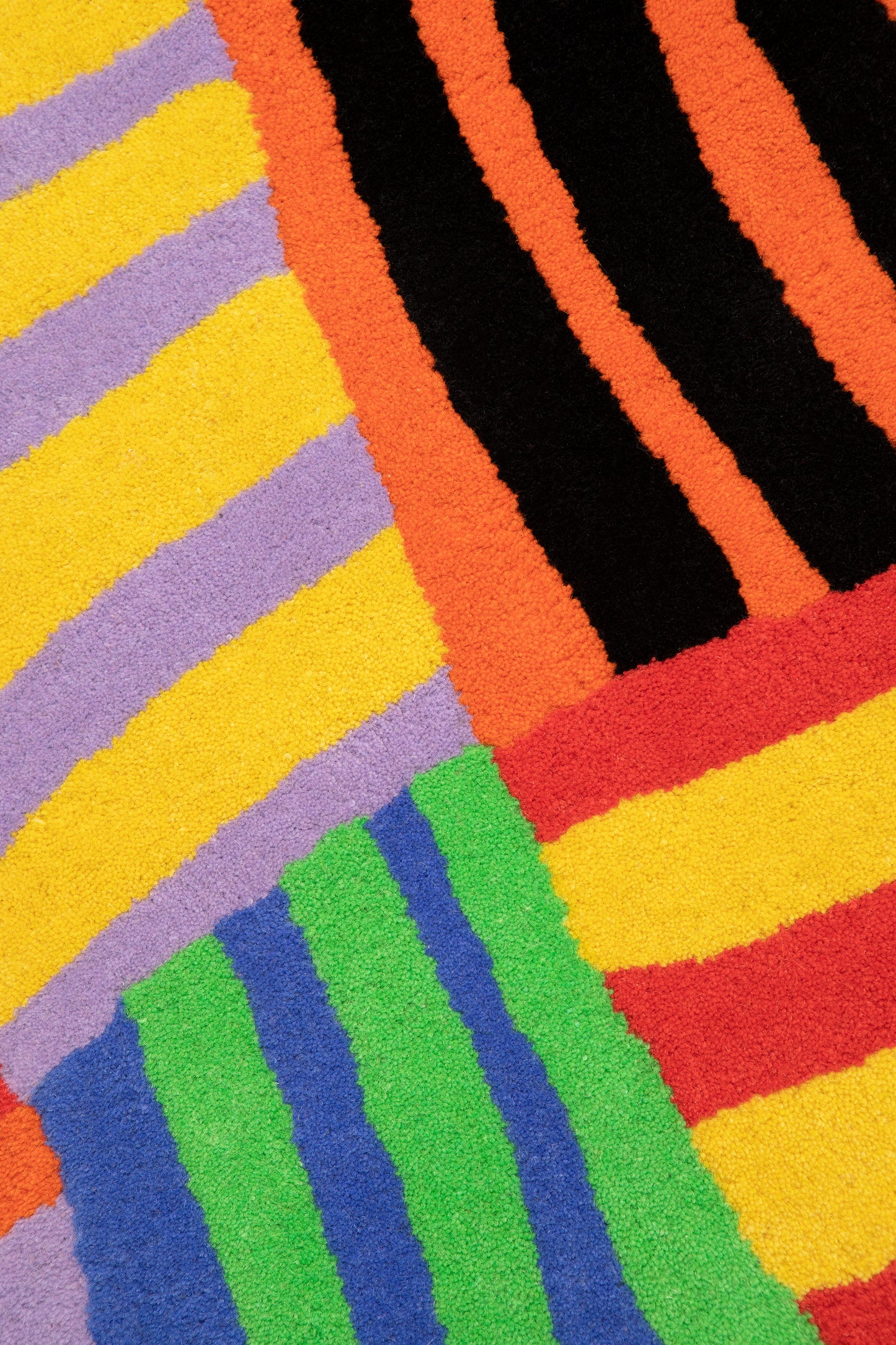 Close up of squiggle stripe rug showing four different stripe groupings- yellow and purple, orange and black, blue and green, and red and yellow. 