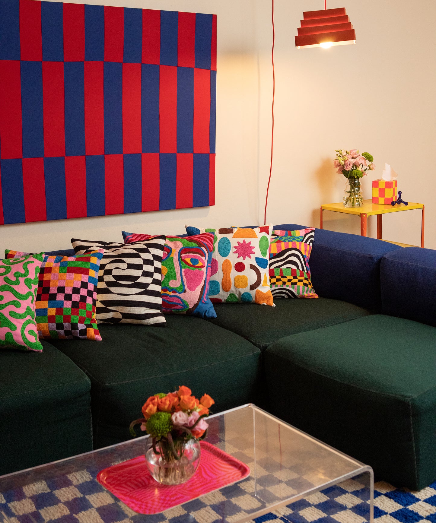 Detail of the Odds and Ends Pillow sitting horizontally across a blue and green couch amongst the five other pillow covers from the 2022 Fall Collection.