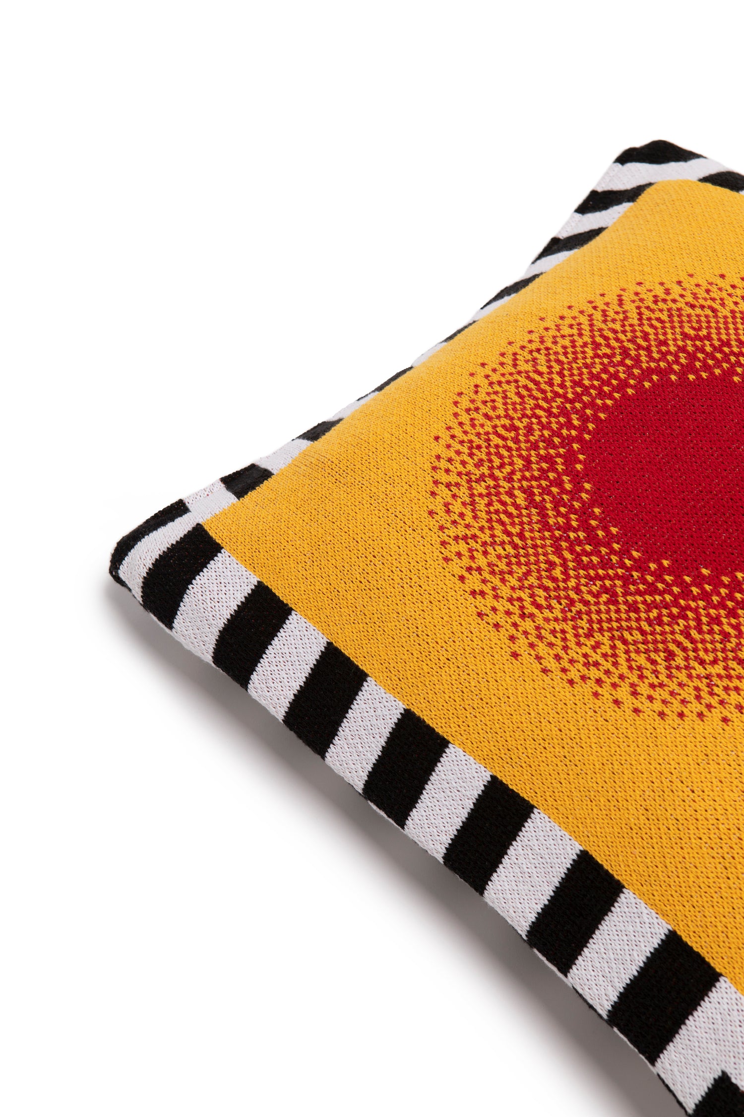 Close up image of burst pillow cover showing the corner of the pillow with the black and white stripe border and a red circle gradually going into a yellow background.