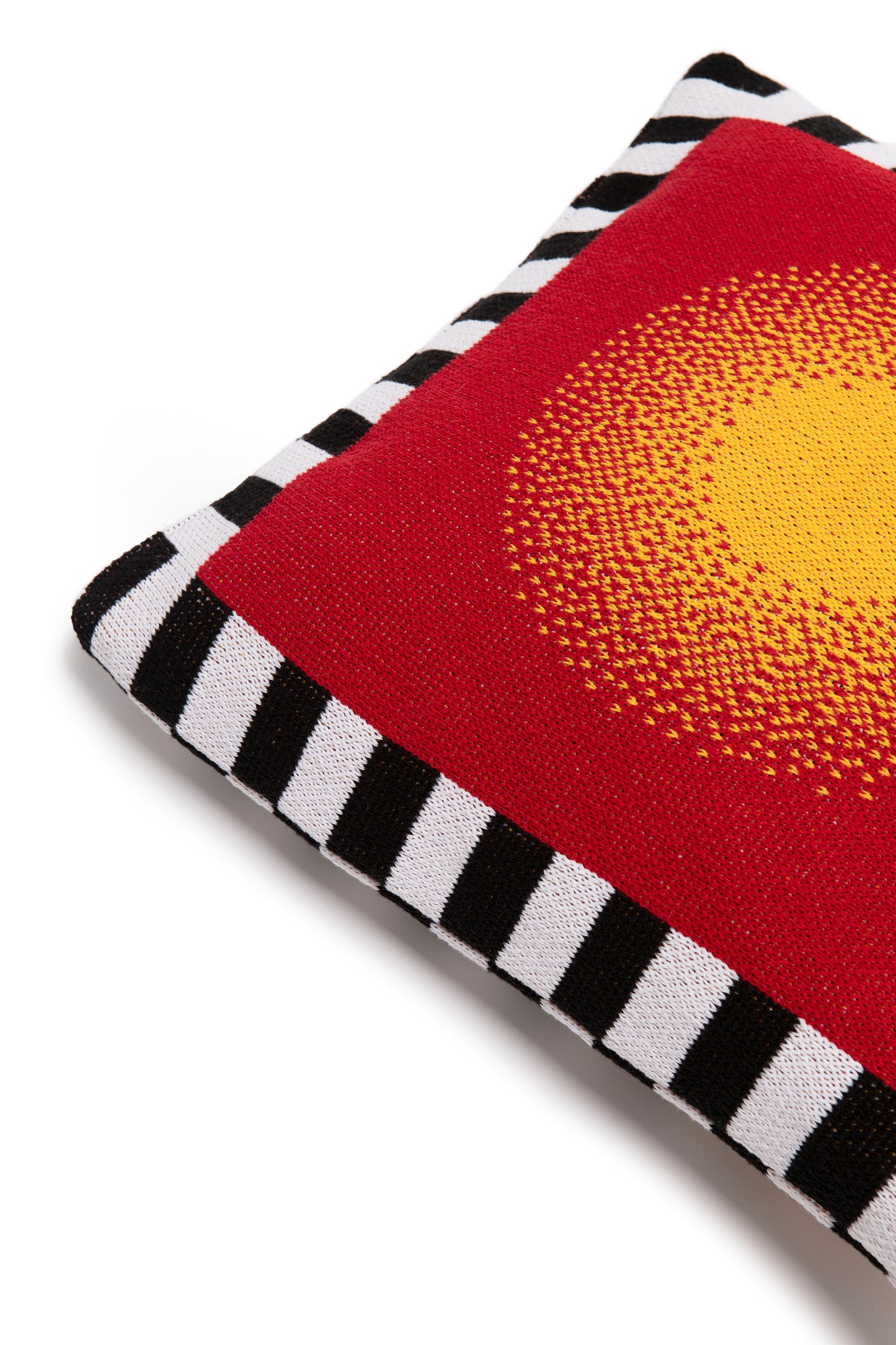 Close up image of burst pillow cover showing the corner of the pillow with the black and white stripe border and a yellow circle gradually going into a red background.