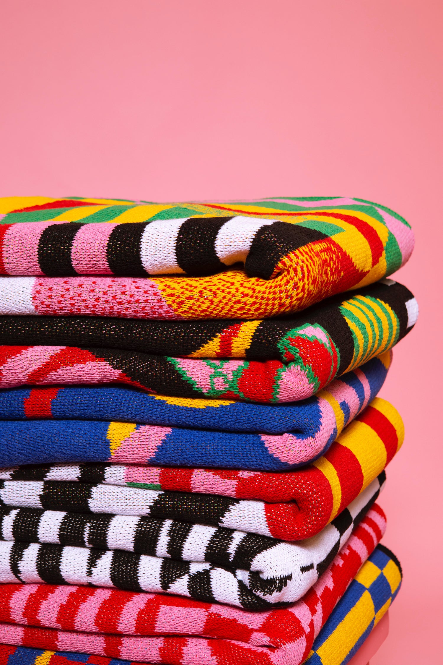 The Dazzle Blanket shown a stack of blankets against a pink ground. This stack is 7 blankets high.