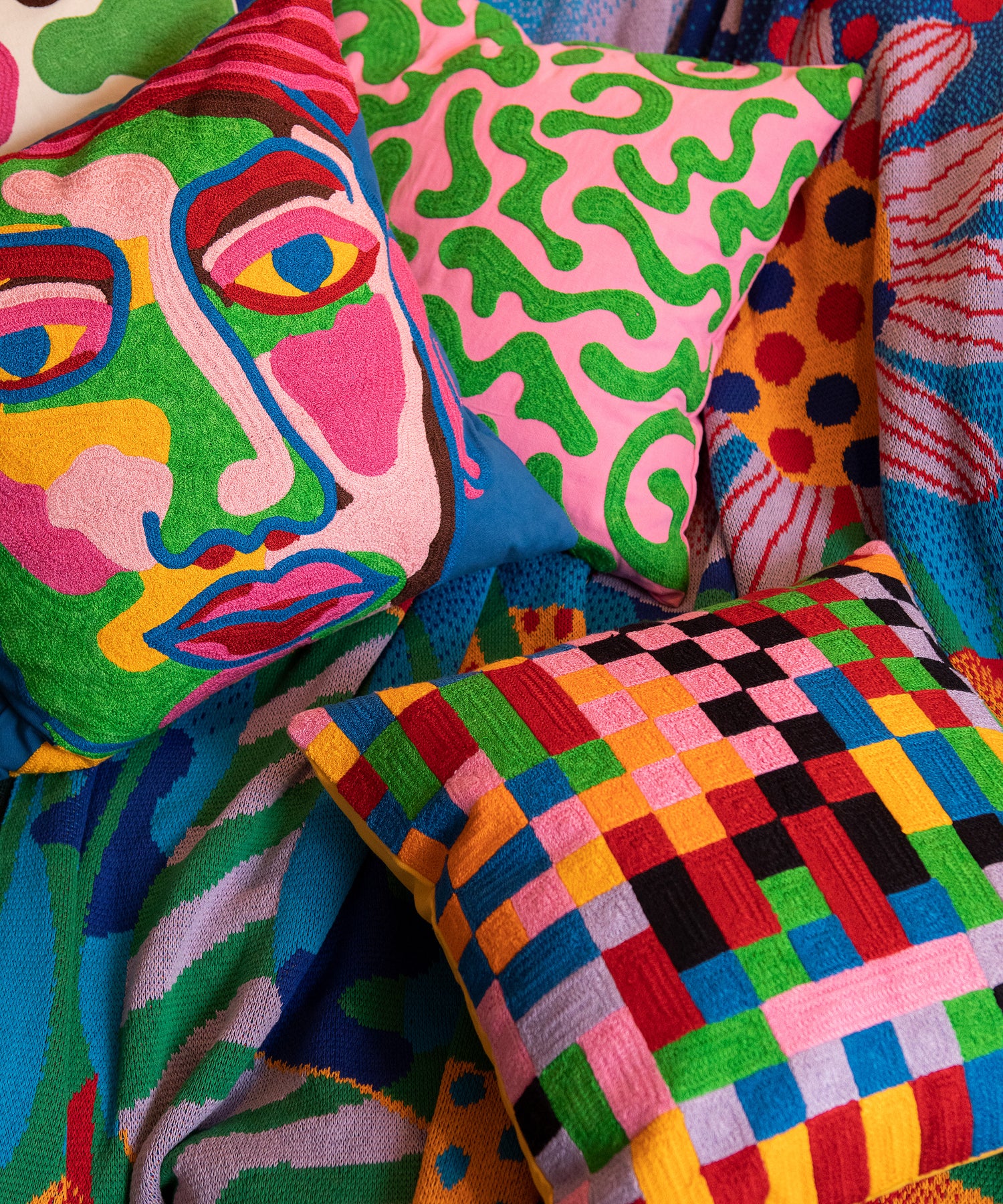 Detail of Silly Squiggles pillow laying on top of the Best Buds Blanket next to the Pixels and Portrait Pillows.