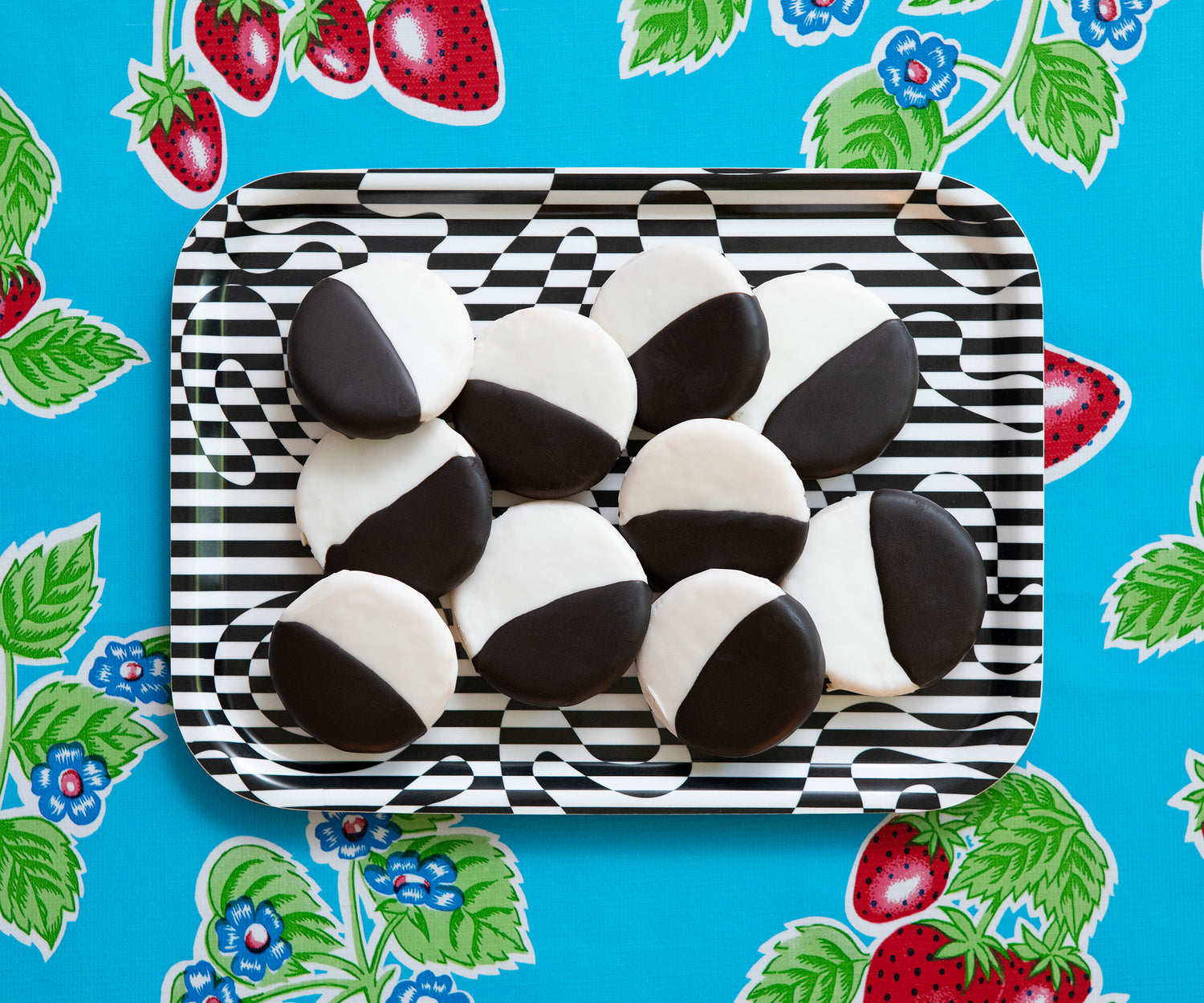 Detail of the Dazzle Tray with black and white cookies filling the tray against a strawberry patterned background. 