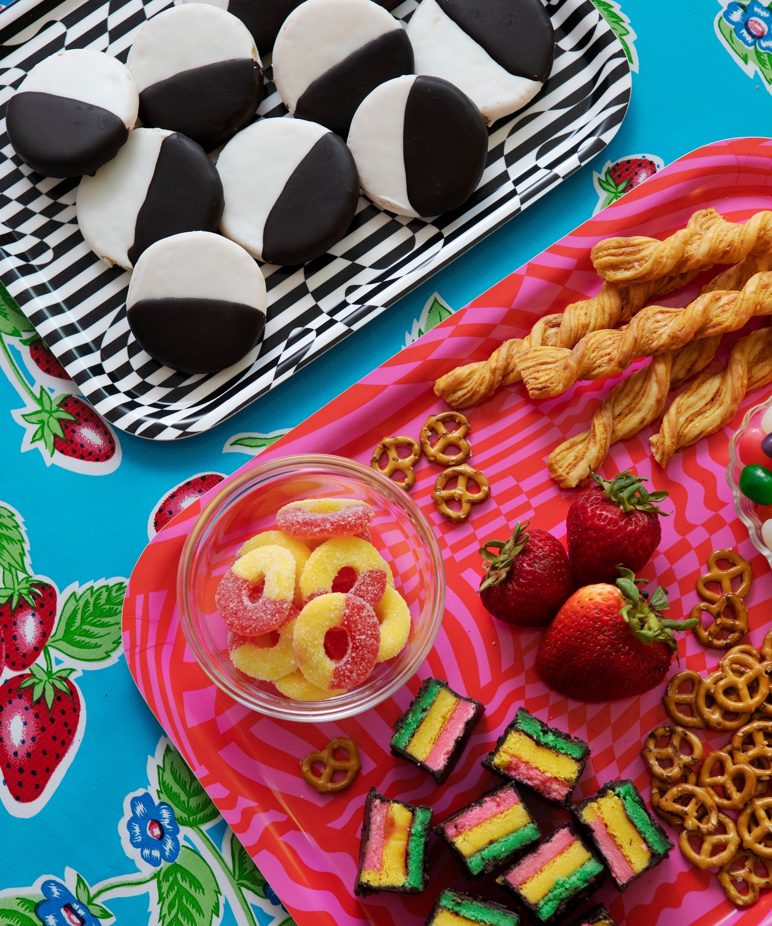 Wiggles and Waves Tray laying next to the Dazzle Tray on a table. The Wiggles and Waves Tray holds peach rings, rainbow cookies, strawberry, and pretzels.