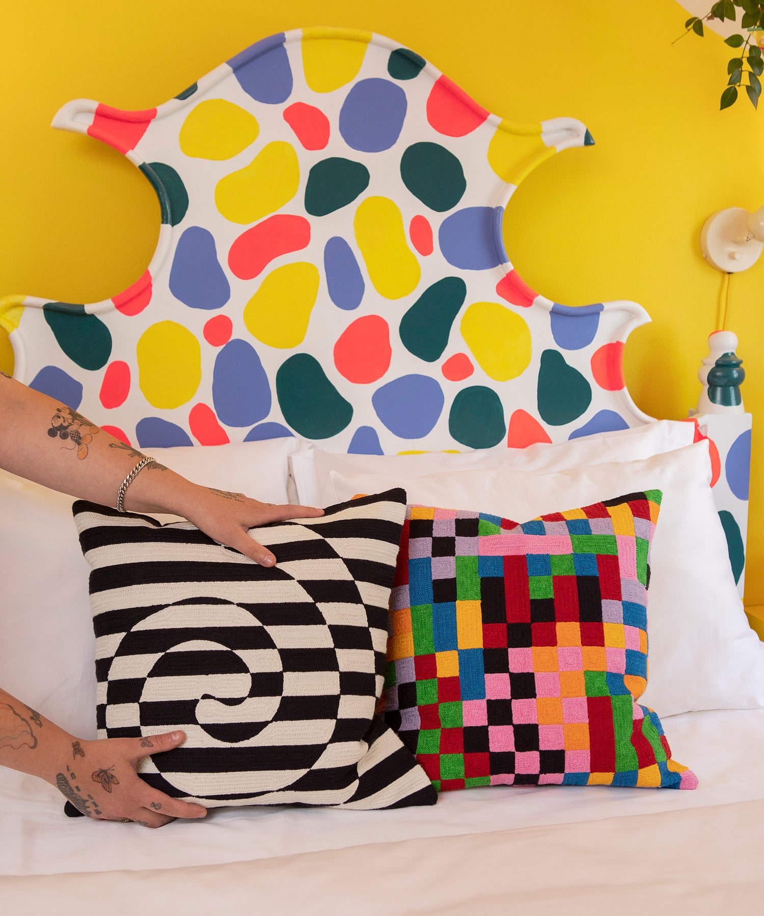 Detail of hands placing the Dazzle Pillow on a made bed next to the Pixels Pillow Cover.
