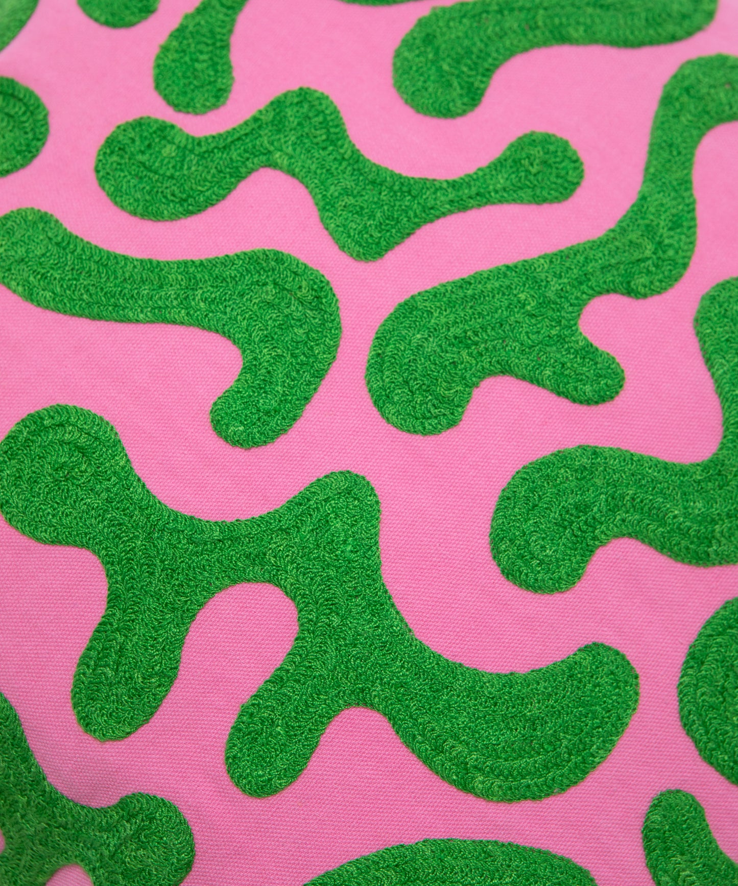 Close up detail of silly squiggle pillow cover showing the stitching in the green squiggle shapes on a pink background.