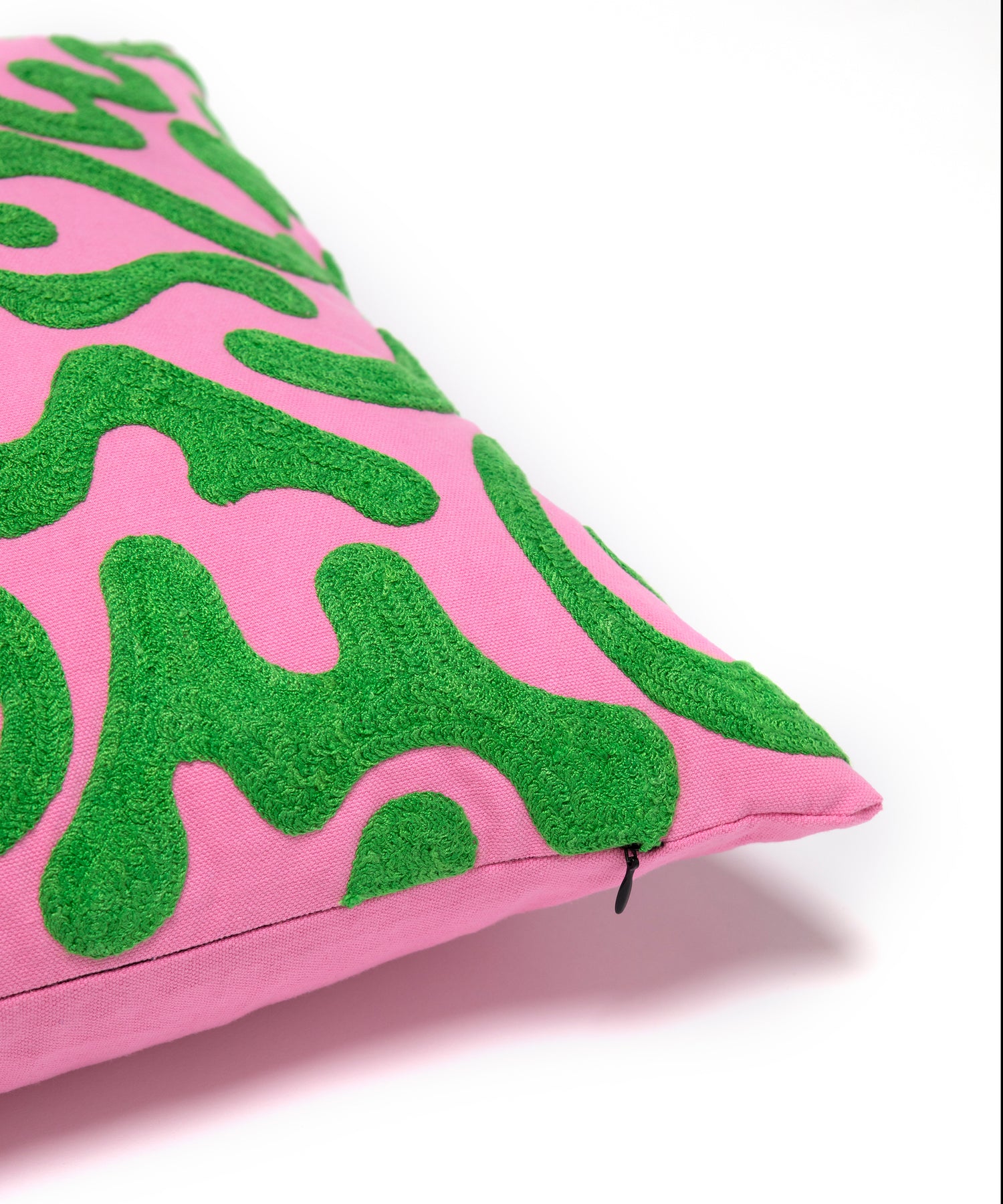 Corner detail of silly squiggle pillow showing green squiggle shapes on it's pink background also showing the zipper enclosure.
